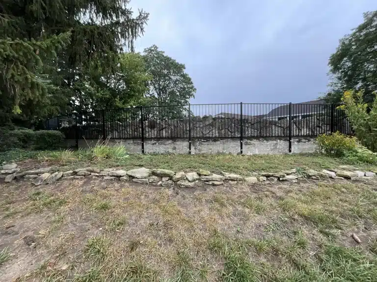 Black ornamental aluminum fence installed along a stone retaining wall in Fort Wayne, Indiana